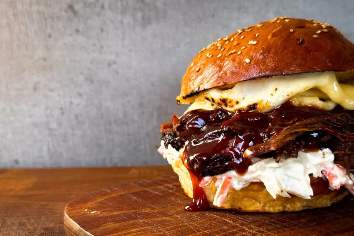 Saftiger pulled beef burger mit geschmolzenem Käse und BBQ-Sauce, serviert auf einem Holzbrett.