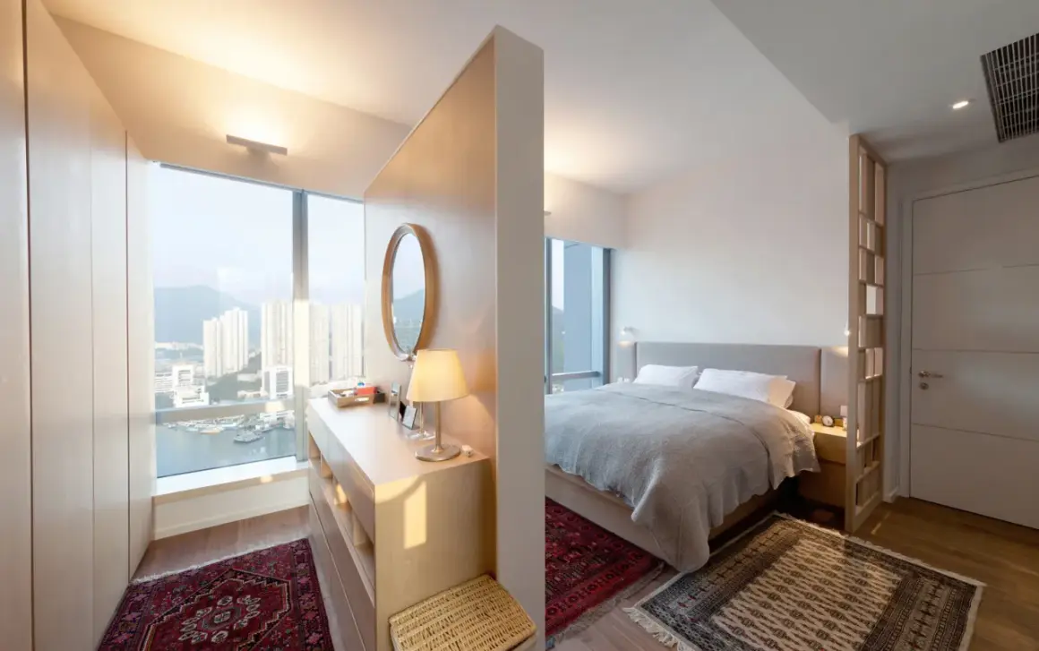 Ein moderner Schlafbereich mit einem Bett, getrennt durch einen eleganten raumteiler vorm bett, der auch als Schminktisch dient.