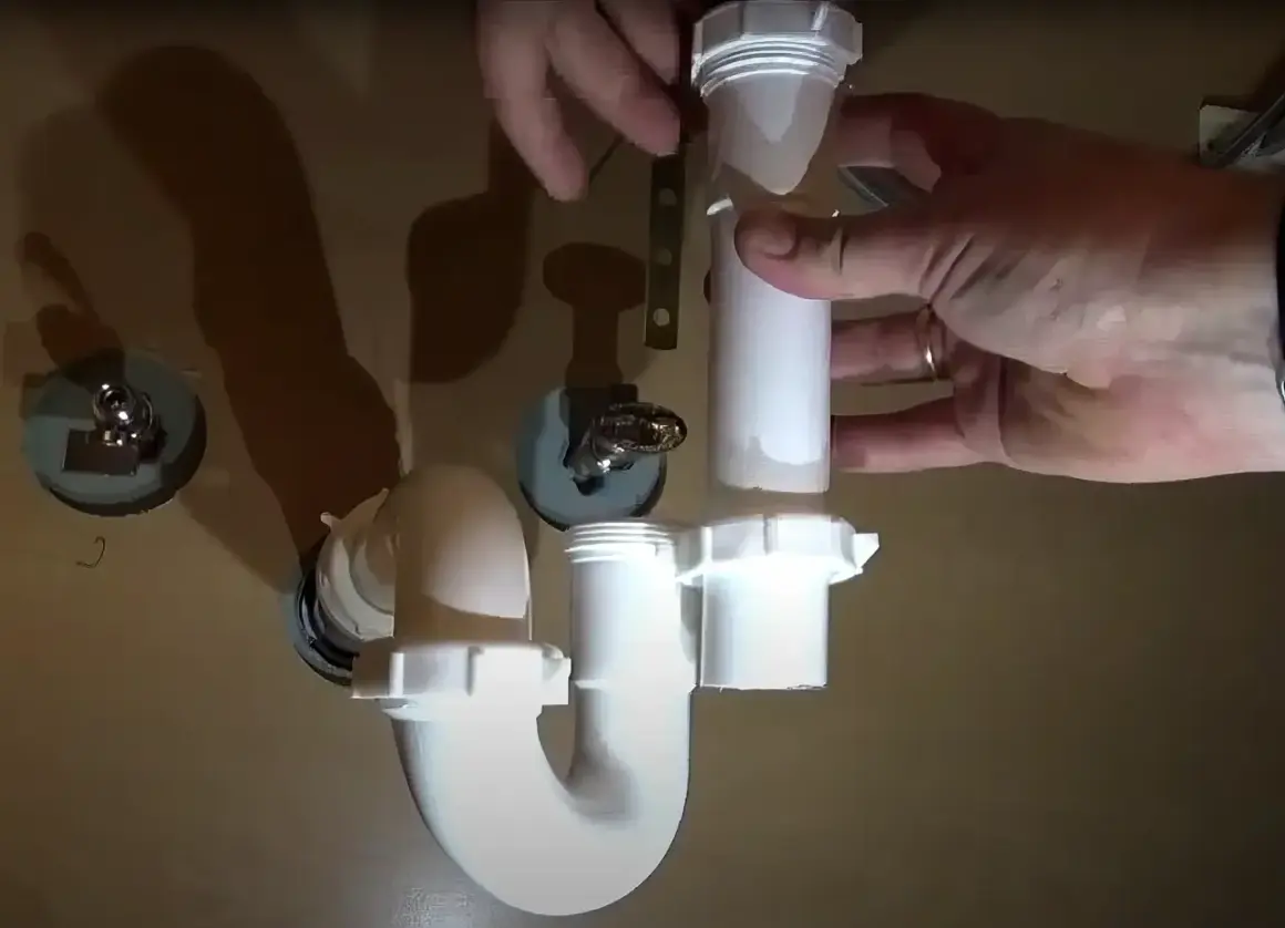 Hands assemble a white P-trap for a kitchen sink installation.