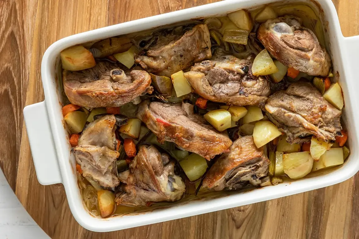 Capretto al forno ricetta della nonna: succulenti pezzi di carne dorata con patate e carote in una teglia bianca.