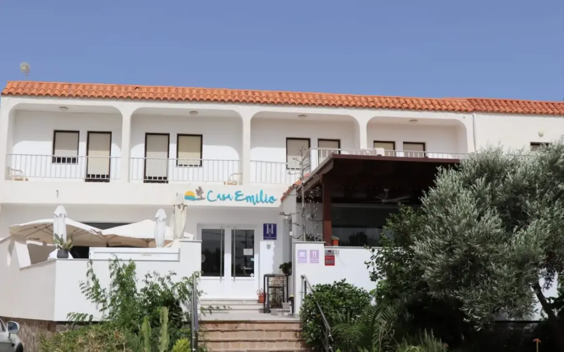 Casa Emilio Los Escullos, un hotel blanco con tejas rojas, balcón y vegetación exuberante.
