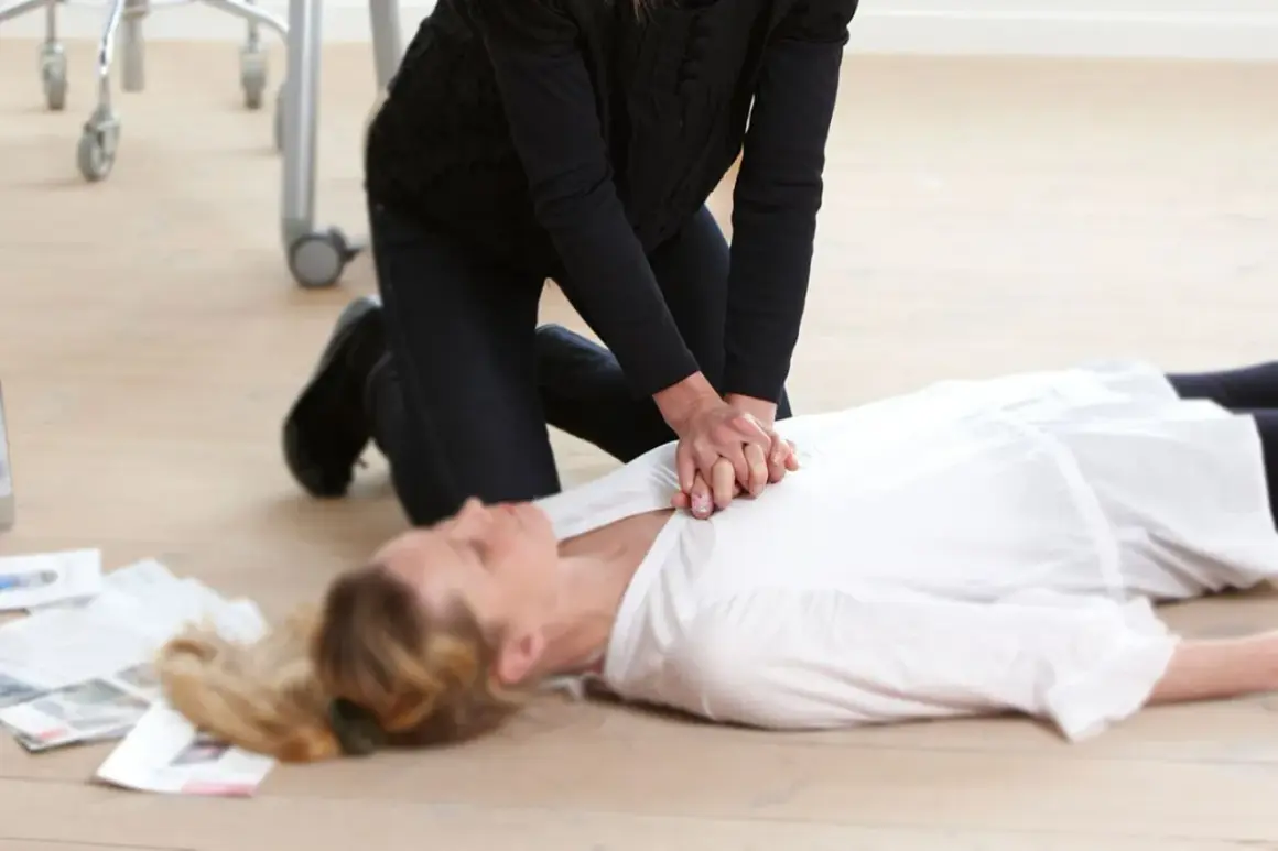 Erste Hilfe bei einem Schlaganfall: Eine Person kniet neben einer liegenden Frau und führt eine Herzmassage durch.