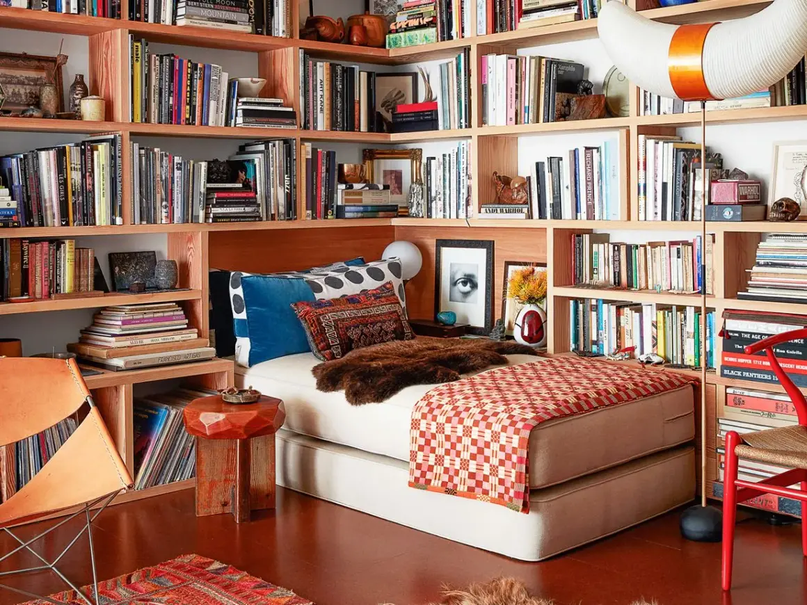 Gemütliches Lesezimmer einrichten mit Bücherregalen voller Bücher, einem Bett, einem Ledersessel und einem roten Stuhl.