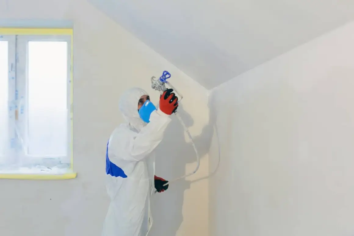 Persona con traje protector y mascarilla pintando paredes con pistola.