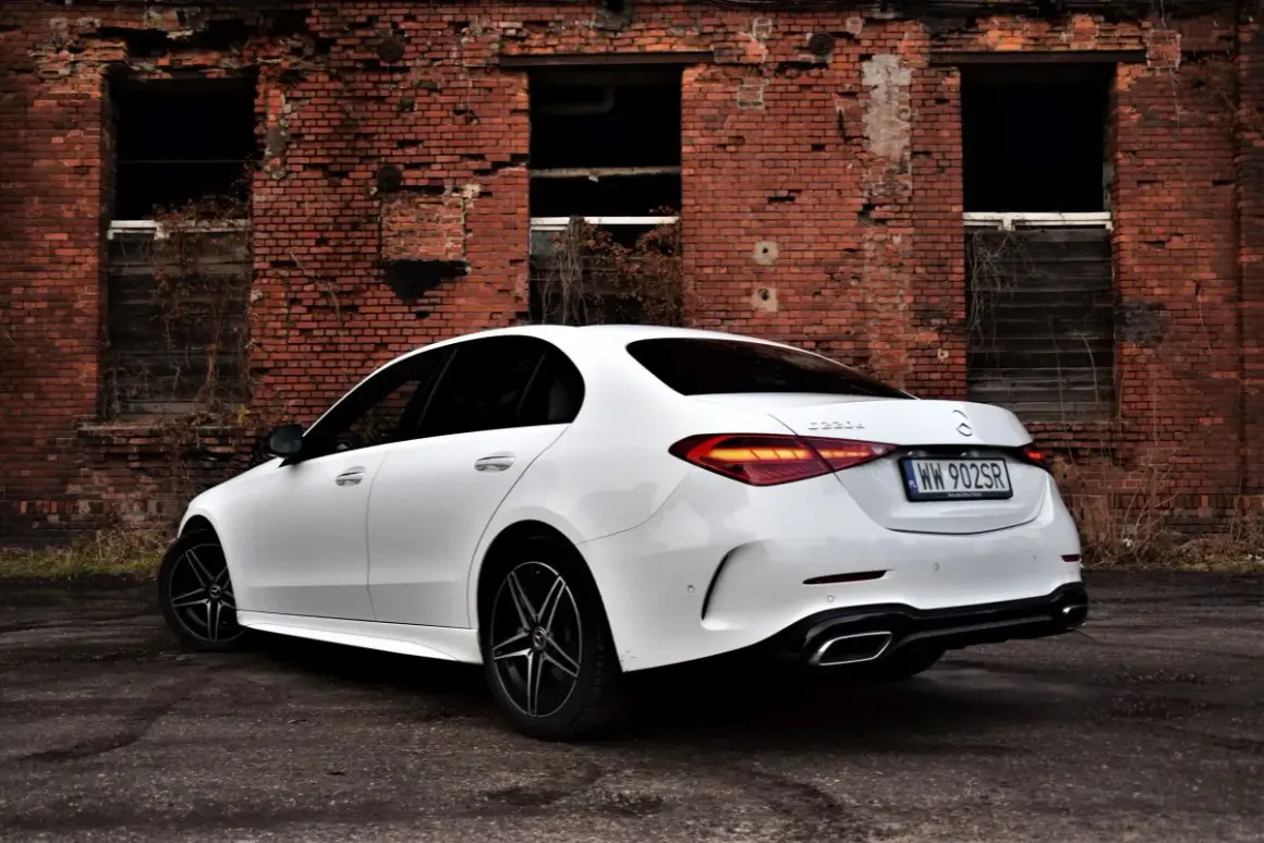 Biały Mercedes C 220 d z czarnymi felgami na tle zrujnowanej ceglanej ściany.
