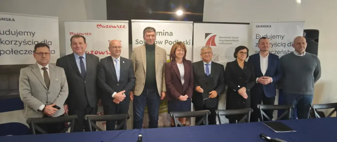 Grupa osób pozuje do zdjęcia na tle banerów informujących o budowie obwodnicy Sokołowa Podlaskiego.