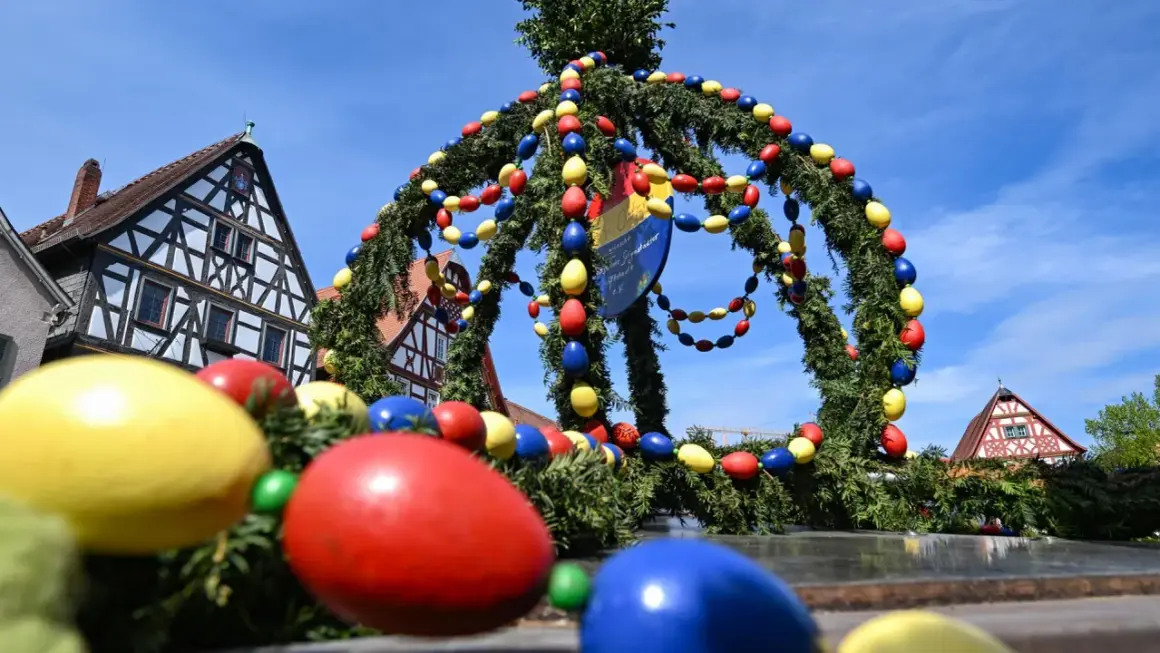 Bunte Ostereier schmücken einen Tannenkranz vor Fachwerkhäusern. Es gibt Karsamstag, die Vorfreude auf Ostern ist spürbar.