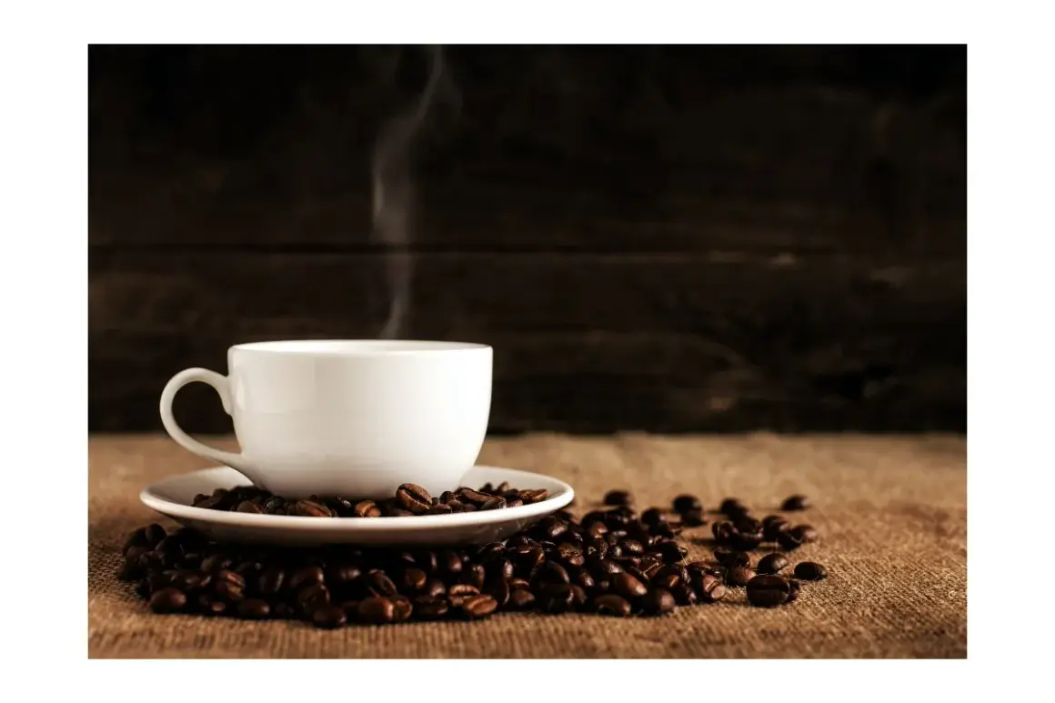 En vit kopp med ångande kaffe står på en hög med kaffebönor. Hur många koppar kaffe per dag är din gräns?