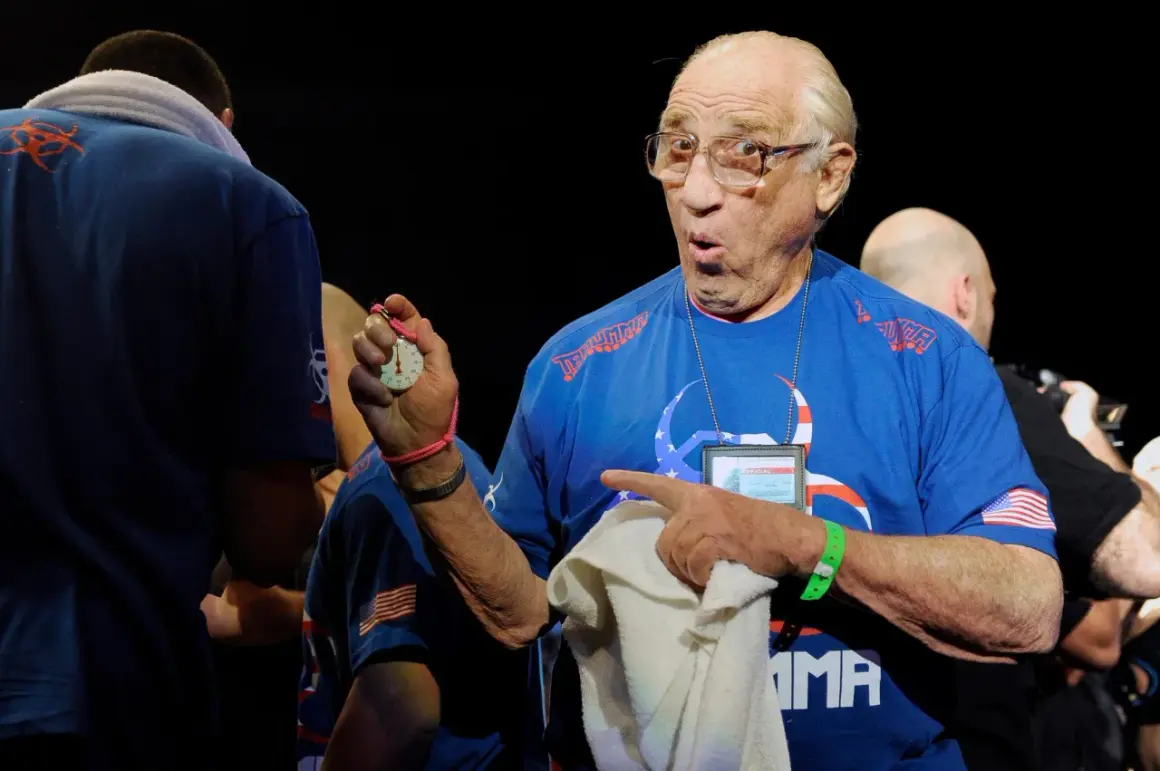 Gene Lebell, med förvånat uttryck, håller upp en tidtagningsklocka och pekar.