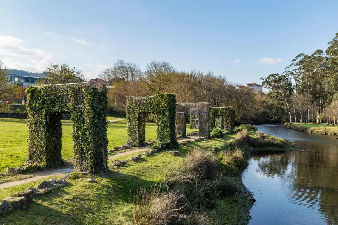 Paseo por la illa das esculturas Pontevedra, con arcos cubiertos de hiedra junto a un río.