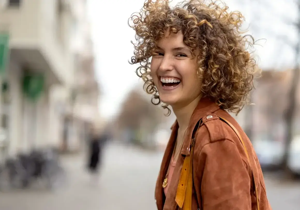Frau mit vollen, lockigen Haaren, die lacht. Perfekt gestylte Locken, die ihr Gesicht umrahmen.