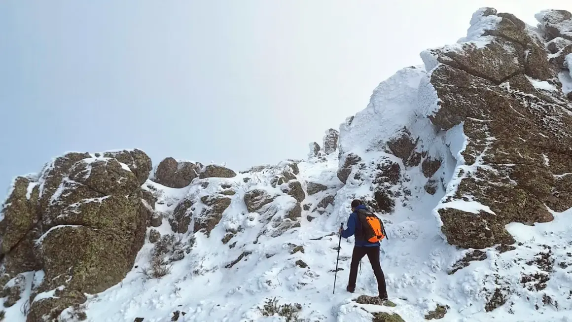 Un excursionista asciende una ladera nevada. Las rocas cubiertas de nieve forman una silueta que recuerda a una montaña con forma de mujer.