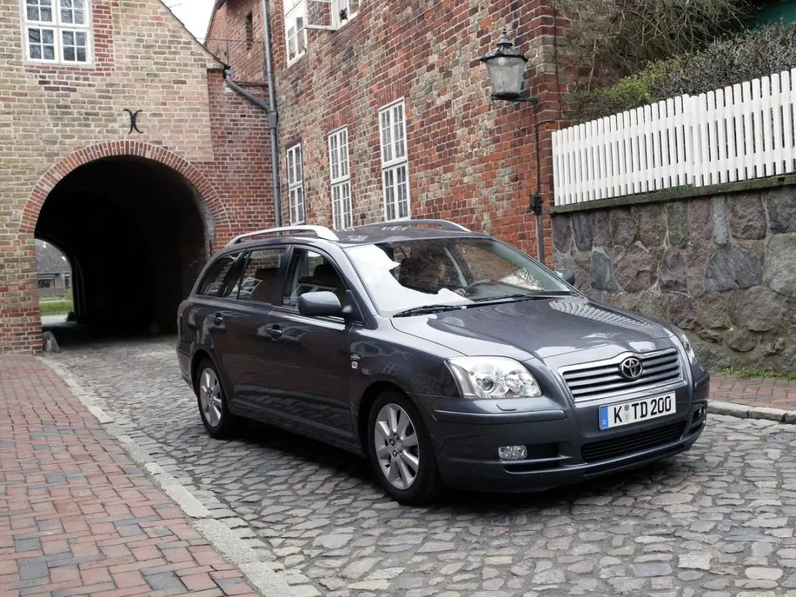 Szary Toyota Avensis T25 2.0 D4D na brukowanej uliczce, obok ceglanego budynku z łukiem.