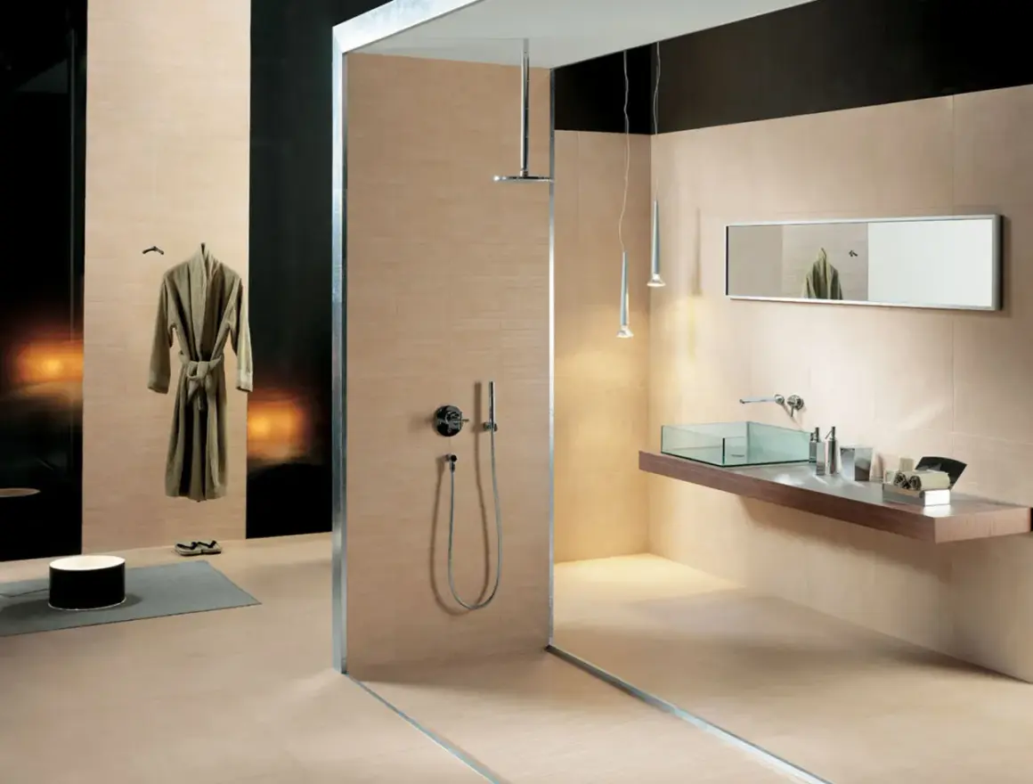 Salle de bain moderne avec douche vitrée, lavabo en verre, miroir et peignoir suspendu. Les carrelages respectent la norme PEI pour une durabilité accrue.