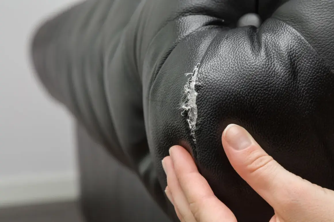 Main d'une personne examinant un accroc sur un fauteuil en cuir noir, montrant la nécessité de réparer le cuir craquelé.