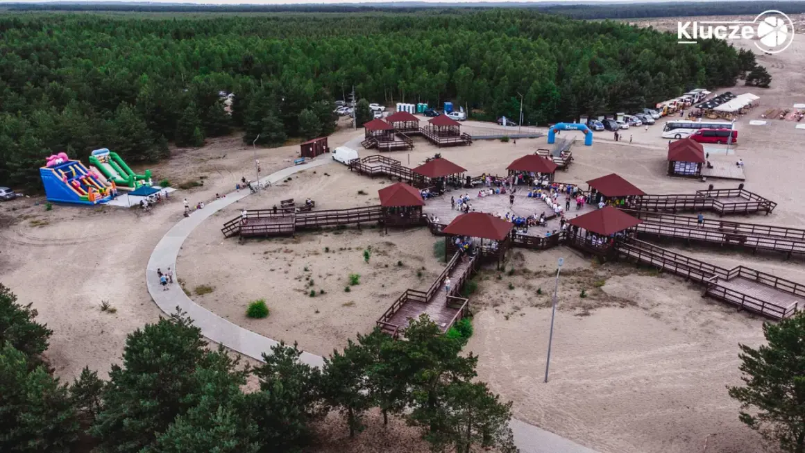 Drewniane zadaszone altany i ścieżki na piaszczystym terenie w miejscowości Klucze, otoczone lasem.