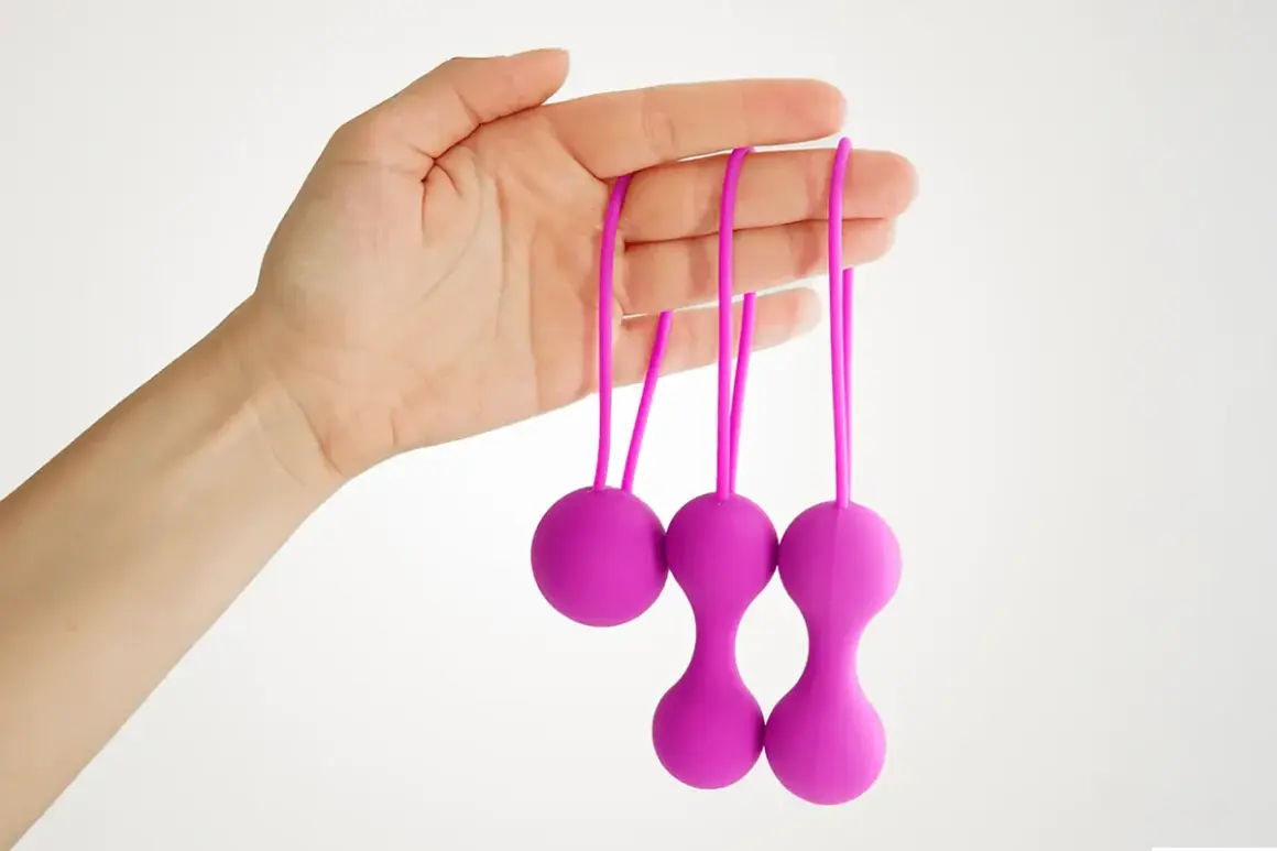 Main d'une femme tenant trois boules de geisha violettes avec des cordons.