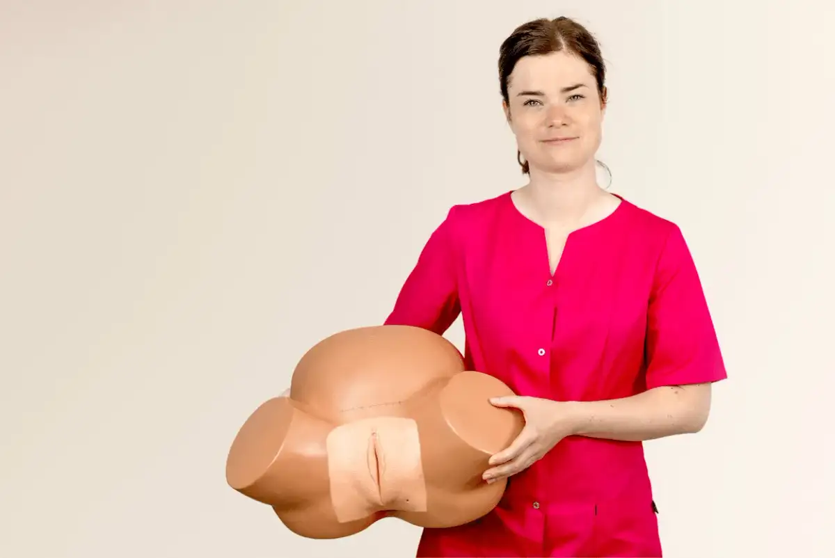 Kobieta w różowej bluzce prezentuje model miednicy do nauki masażu krocza przed porodem.