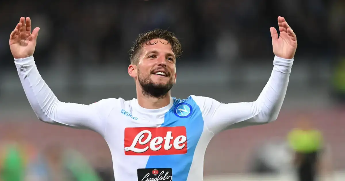 Uśmiechnięty Dries Mertens w białej koszulce Napoli z rękami uniesionymi w geście radości.