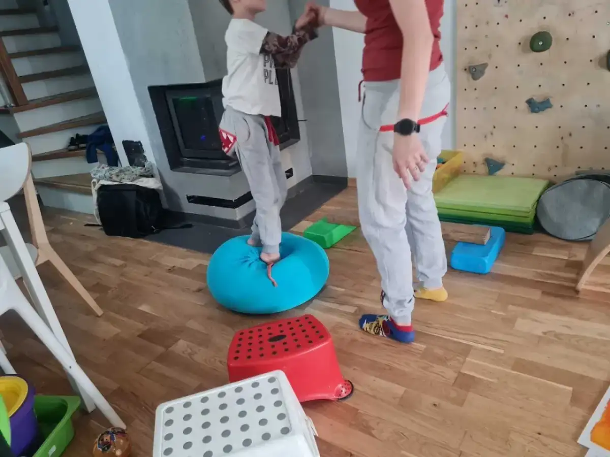 Dziecko ćwiczy równowagę na niebieskiej poduszce, część domowej ścieżki sensorycznej dla dzieci.