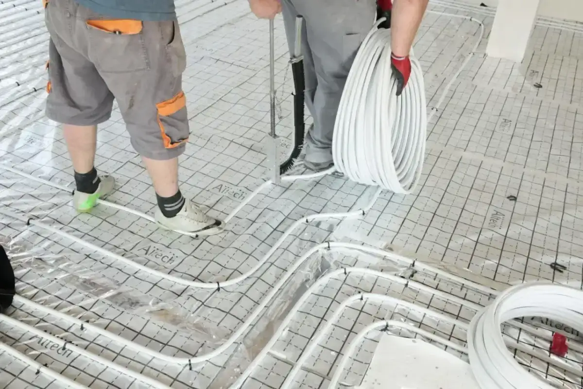 Pracownicy układają rury do ogrzewania podłogowego na siatce. Wkrótce powstanie tu szlichta, która zapewni komfort cieplny.