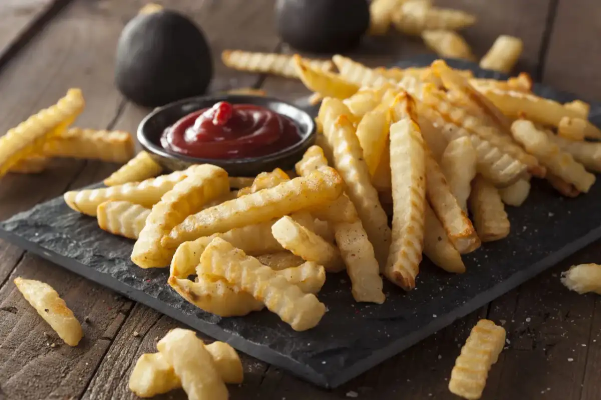 Chrupiące, mrożone frytki z piekarnika, podane z ketchupem na czarnej desce. Idealna przekąska.