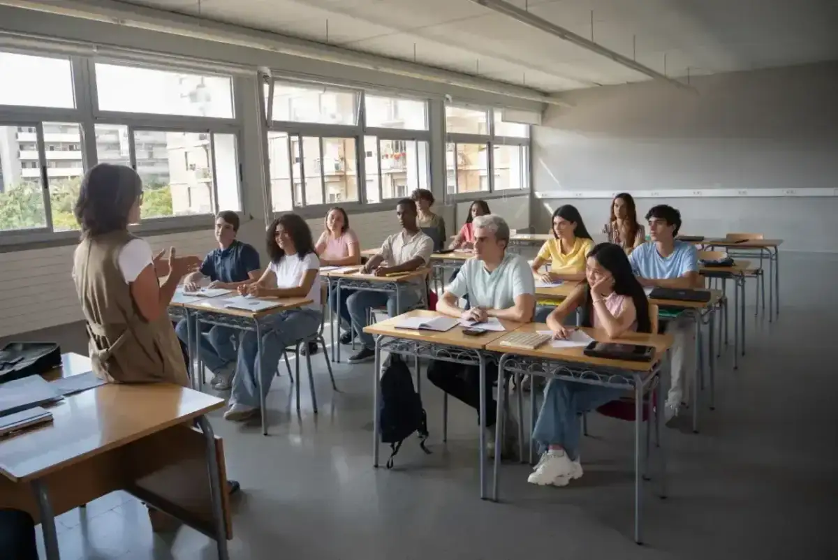 Nauczycielka prowadzi lekcję wychowania do życia w rodzinie. Uczniowie uważnie słuchają, siedząc w ławkach.