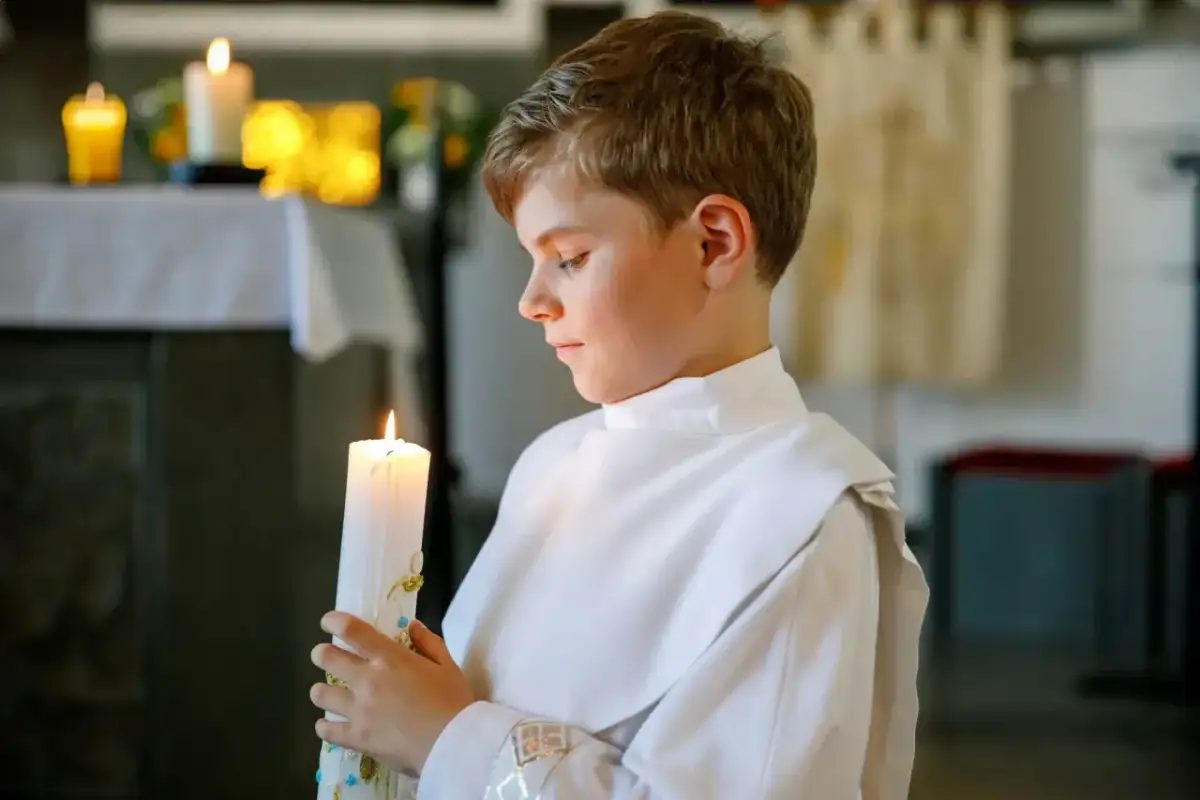 Chłopiec w bieli trzyma zapaloną świecę podczas uroczystości chrztu świętego.