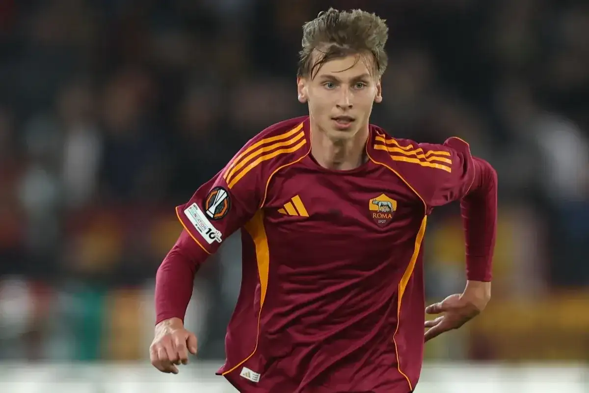 Piłkarz AS Roma w bordowej koszulce z żółtymi pasami, gotowy do gry przeciwko Genoa CFC.
