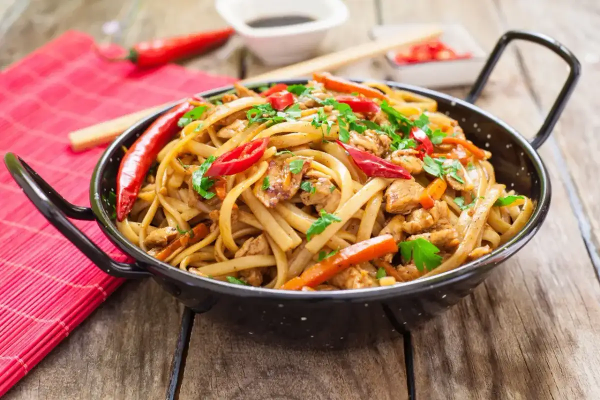 Pyszny makaron chain main z kurczakiem, papryką i chili, posypany natką pietruszki, w czarnej woku.