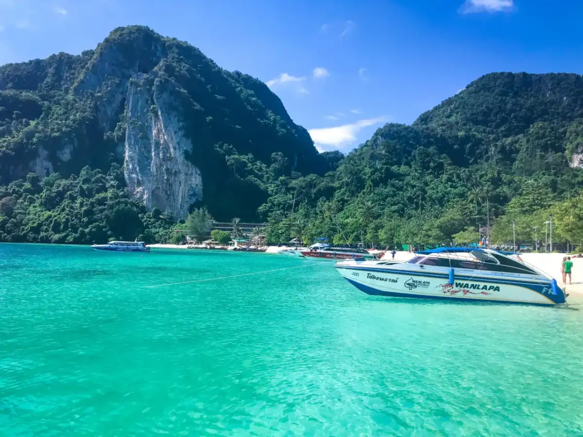 Turkusowa woda i łodzie motorowe przy plaży w Maya Bay. W tle zielone, skaliste góry.