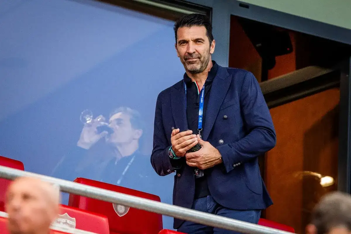 Gianluigi Buffon, legendarny włoski bramkarz, w eleganckim granatowym garniturze, obserwuje mecz z trybun.