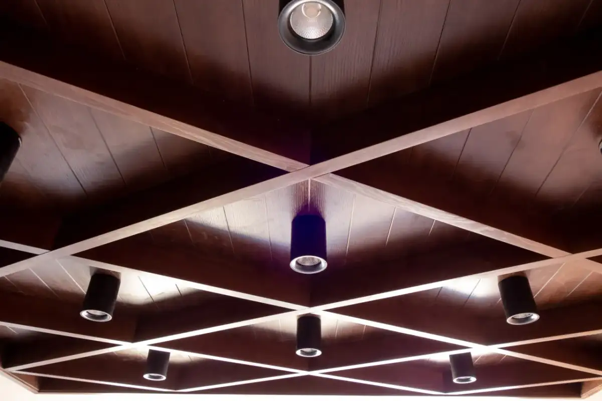 Drewniane, kratownicowe **stare kasetony na suficie** z wbudowanymi reflektorami tworzą geometryczny wzór.