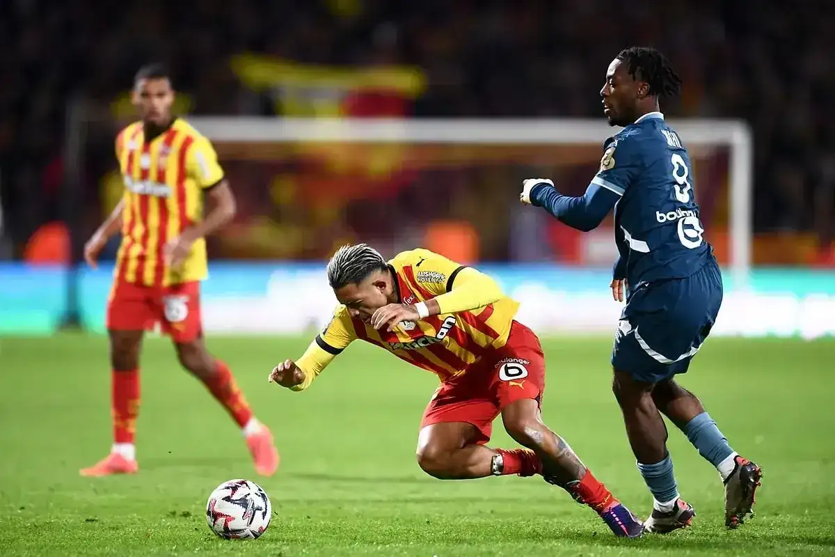 Piłkarz RC Lens w żółto-czerwonym stroju walczy o piłkę z zawodnikiem Stade Rennais.