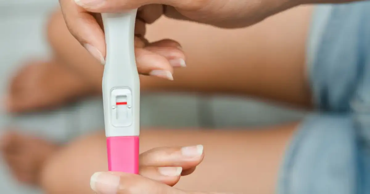 Dłoń trzyma test ciążowy z jedną czerwoną kreską. Kiedy zrobić test ciążowy? Najlepiej po terminie spodziewanej miesiączki.
