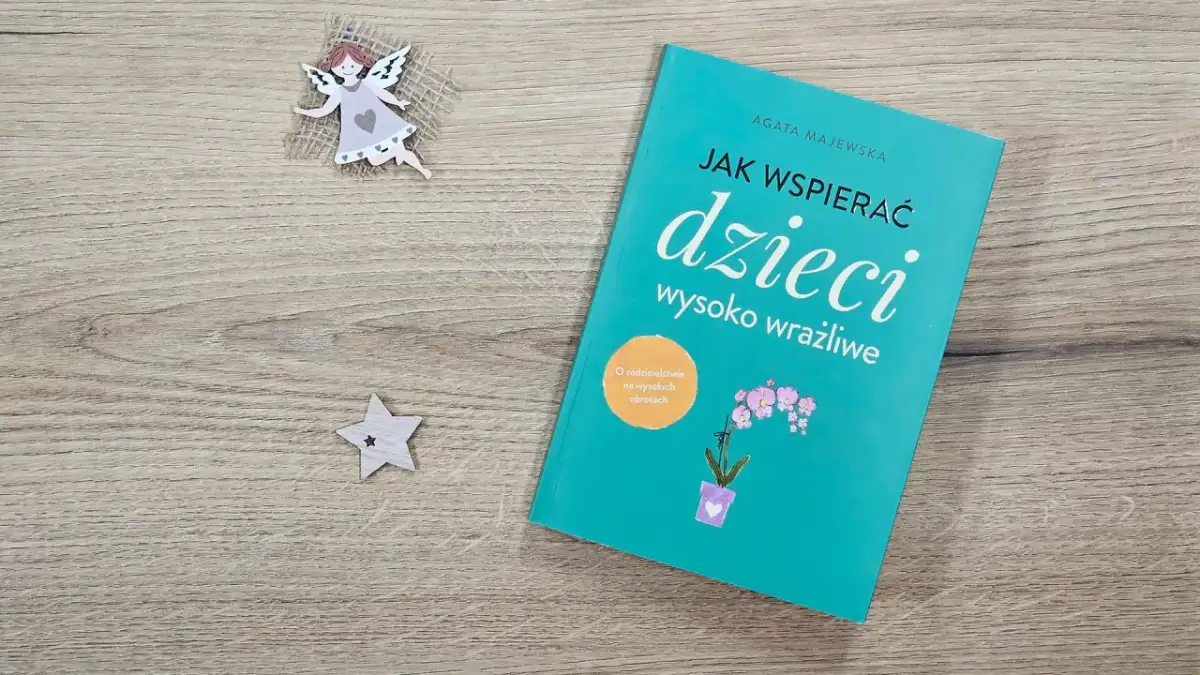 Książka "Jak wspierać dzieci wysoko wrażliwe" na drewnianym tle, obok aniołka i gwiazdki.