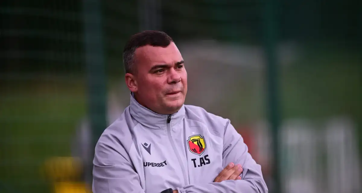 Trener Jagiellonii, z rękami skrzyżowanymi na piersi, w szarej kurtce z herbem klubu.