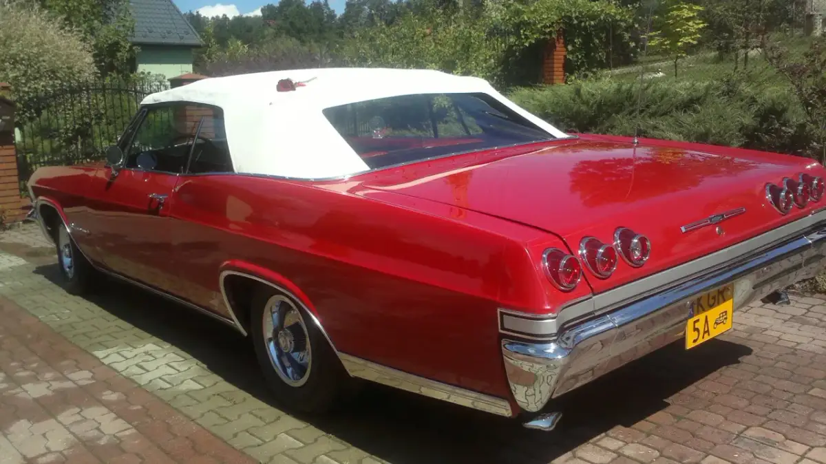 Czerwona kabrioletowa Chevy Impala z białym dachem, zaparkowana na podjeździe z kostki brukowej.