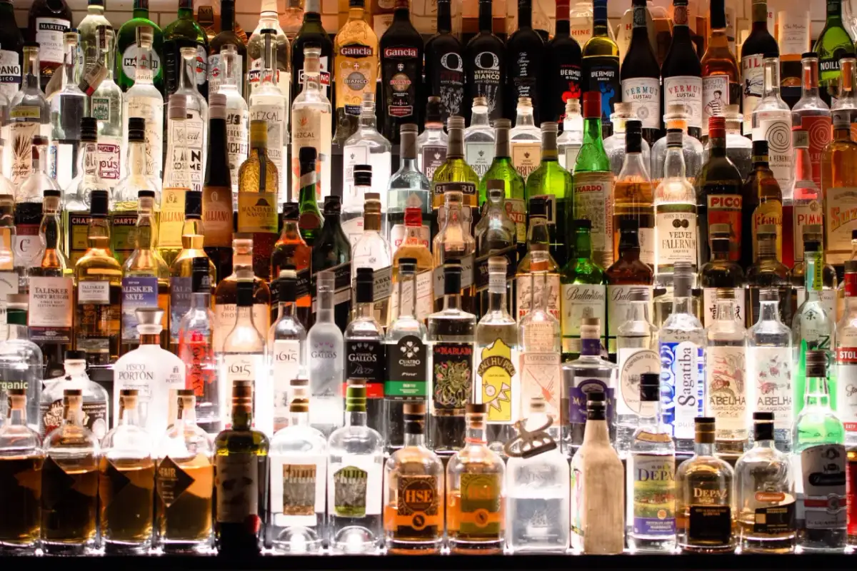Rząd butelek alkoholi, w tym wódki, whisky i likierów, na półce.