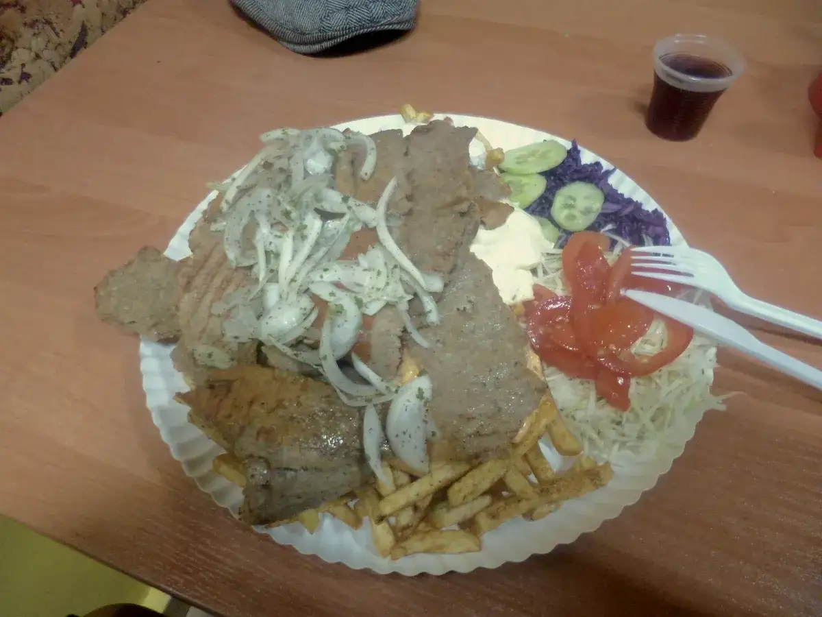 Talerz z kebabem, frytkami, warzywami i napojem.