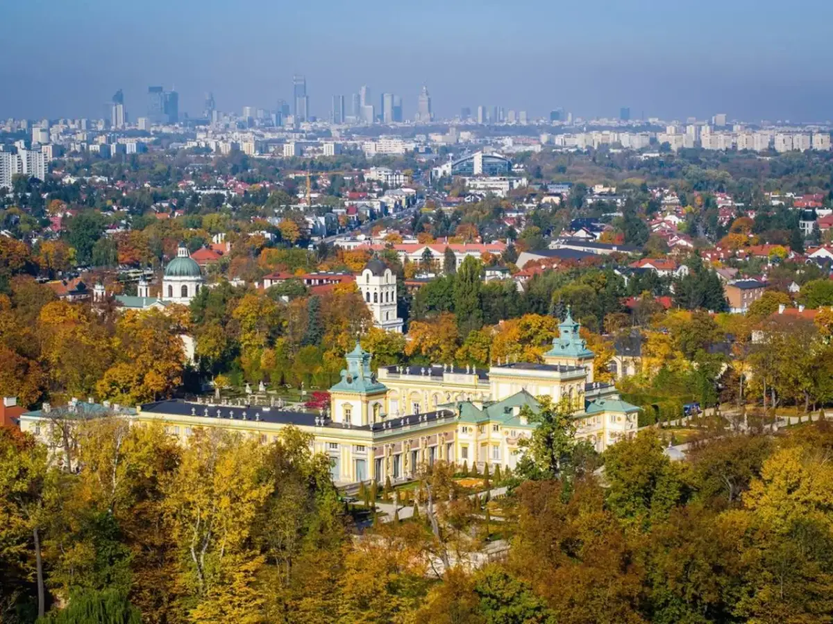 Pałac wilanowski otoczony jesiennym parkiem, z panoramą Warszawy w tle. To symbol najbogatszej dzielnicy Warszawy.