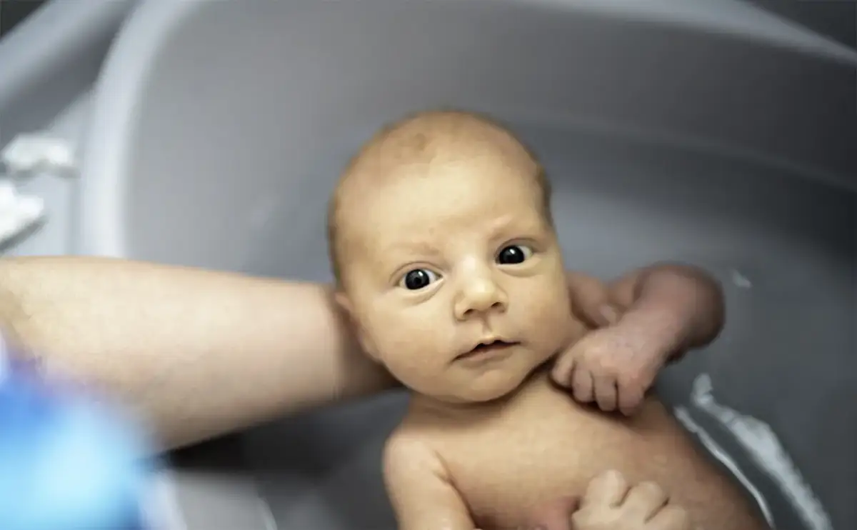 Niemowlę w wanience, z zaciekawieniem patrzy na świat. Czy można kąpać dziecko po szczepieniu? Tak, jeśli nie ma przeciwwskazań lekarza.