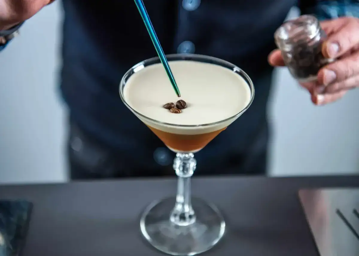 Barista dodaje ziarna kawy do drinka z pianką, przypominającego Espresso Martini. To właśnie Kahlúa nadaje mu ten wyjątkowy, kawowy smak.