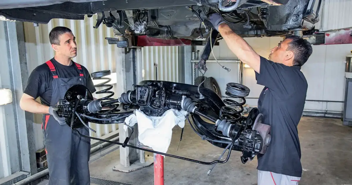 Mechanicy pracują nad zarabianiem przewodów hamulcowych przy podniesionym zawieszeniu samochodu.