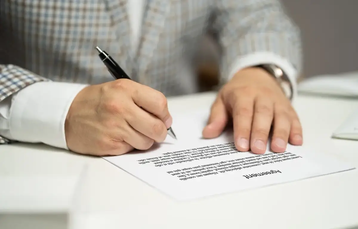 Mężczyzna w garniturze podpisuje umowę kredytową, składając ważny podpis na dokumencie.