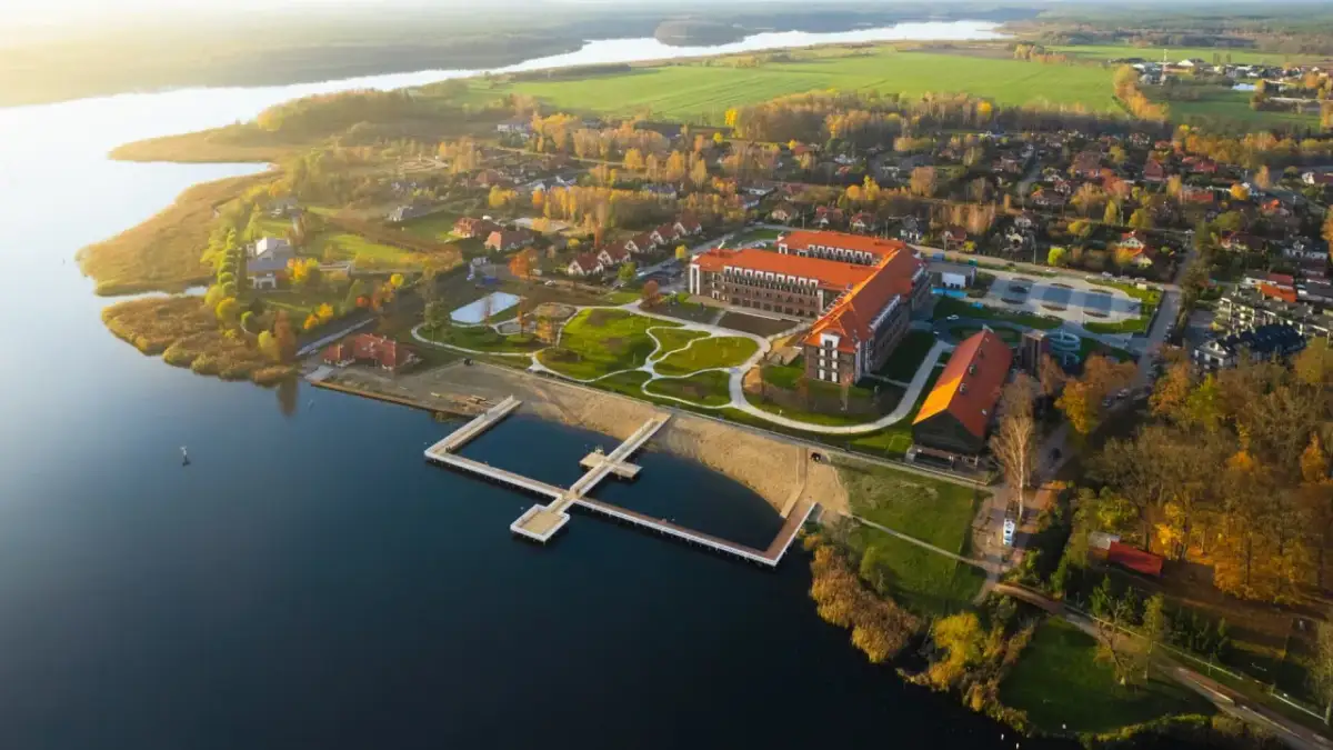 Widok z lotu ptaka na kompleks Lake Hill Mazury z jeziorem, plażą, molo i budynkami w jesiennej scenerii.
