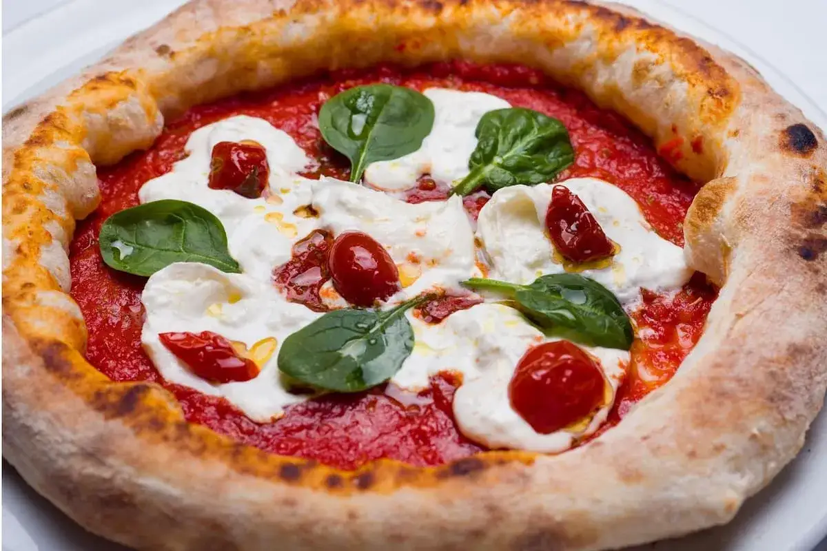 Deliciosa masa de pizza napolitana con tomate, mozzarella fresca, tomates cherry y hojas de albahaca.
