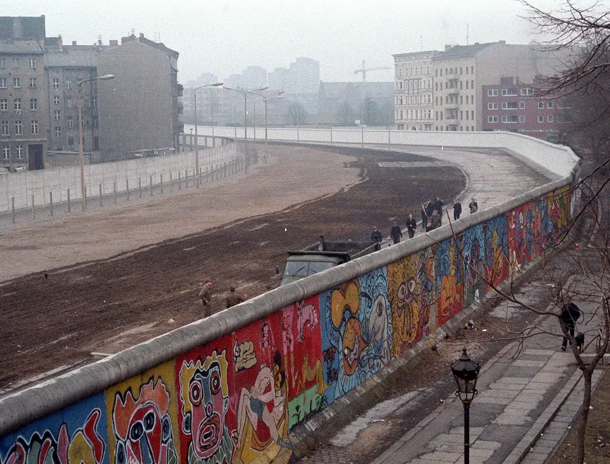 Kolorowy mur berliński, świadectwo czasów, kiedy zbudowano mur berliński, z ludźmi spacerującymi po jego drugiej stronie.