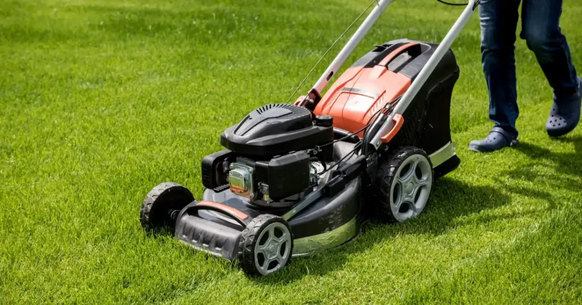 Osoba prowadzi kosiarkę rotacyjną spalinową po soczyście zielonym trawniku.