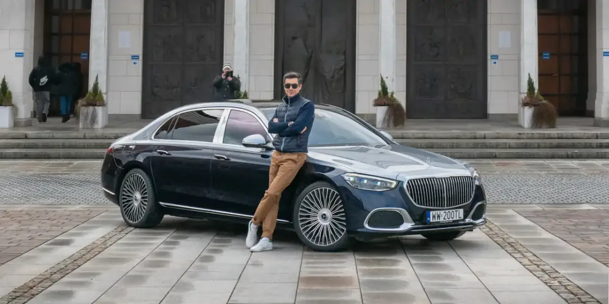 Elegancki mężczyzna opiera się o lśniącego Maybacha S580 przed monumentalnym budynkiem.